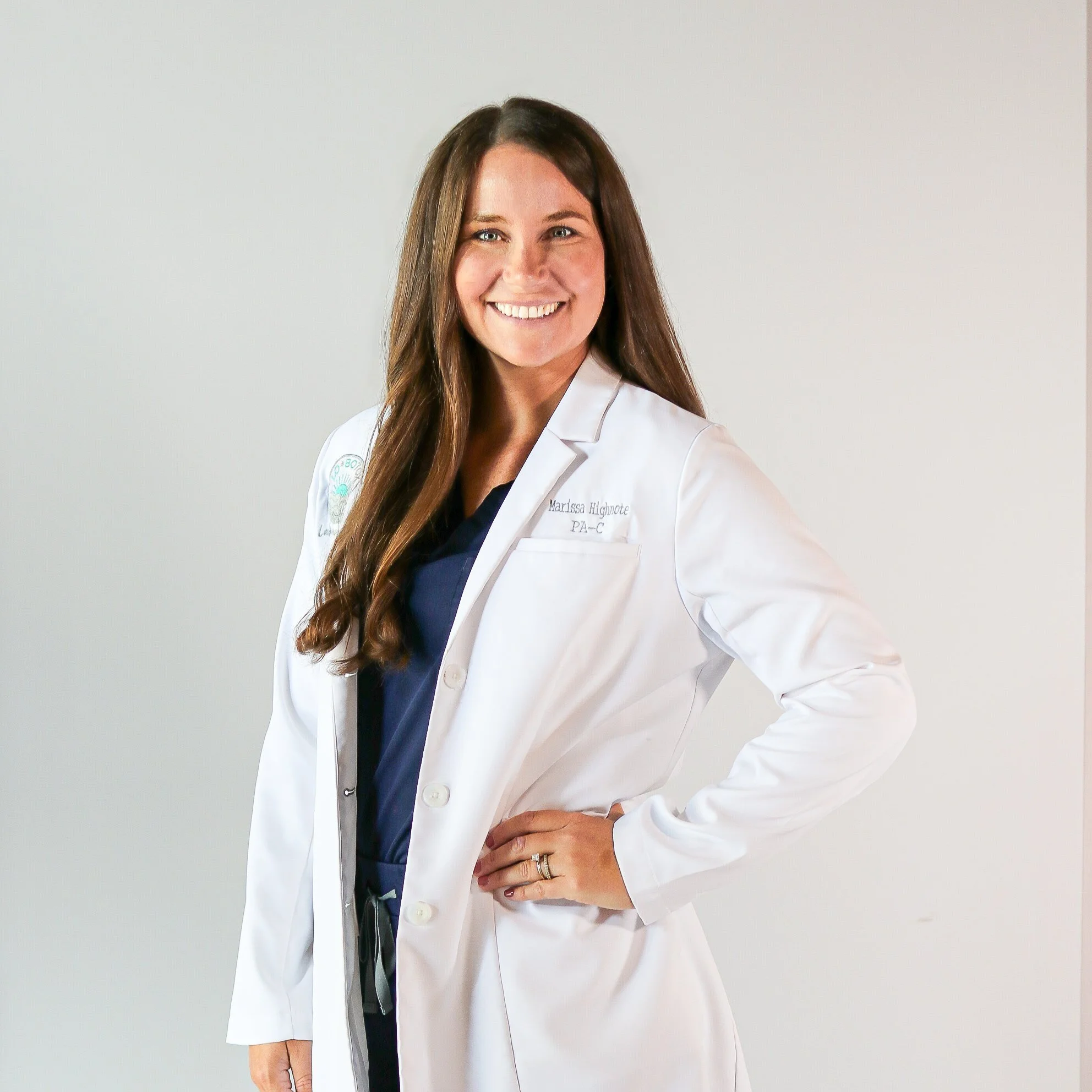 Portrait of a female doctor in a white coat, smiling, against a plain background.