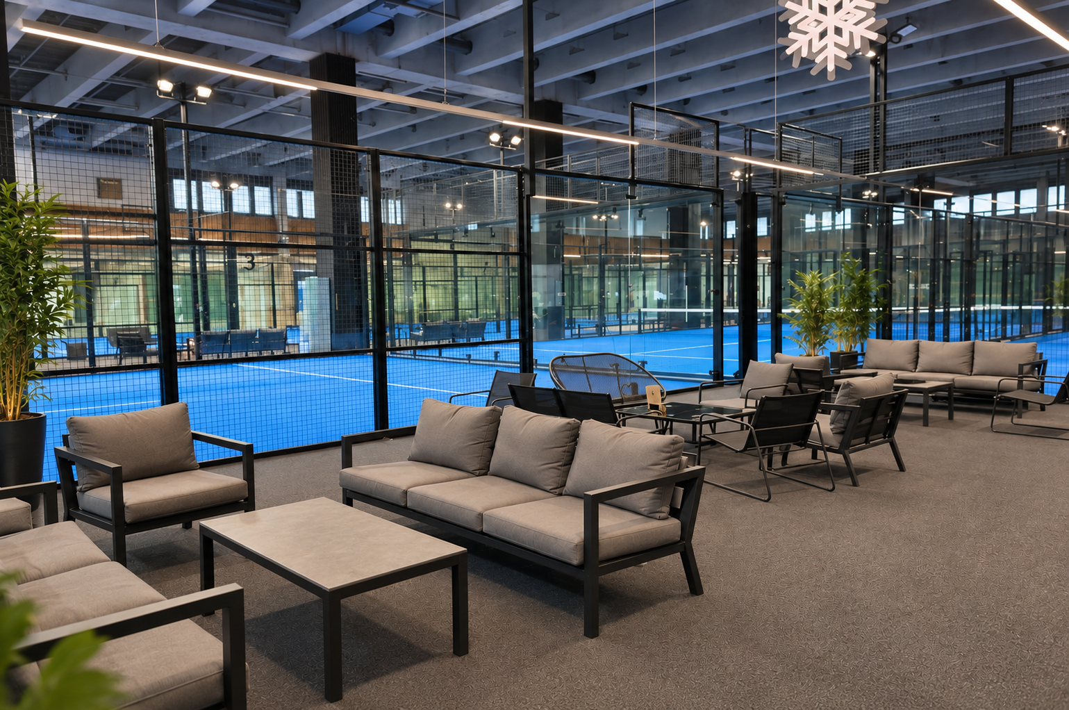 Indendørs lounge med siddepladser og store vinduer, der viser en indendørs tennisbane udenfor.