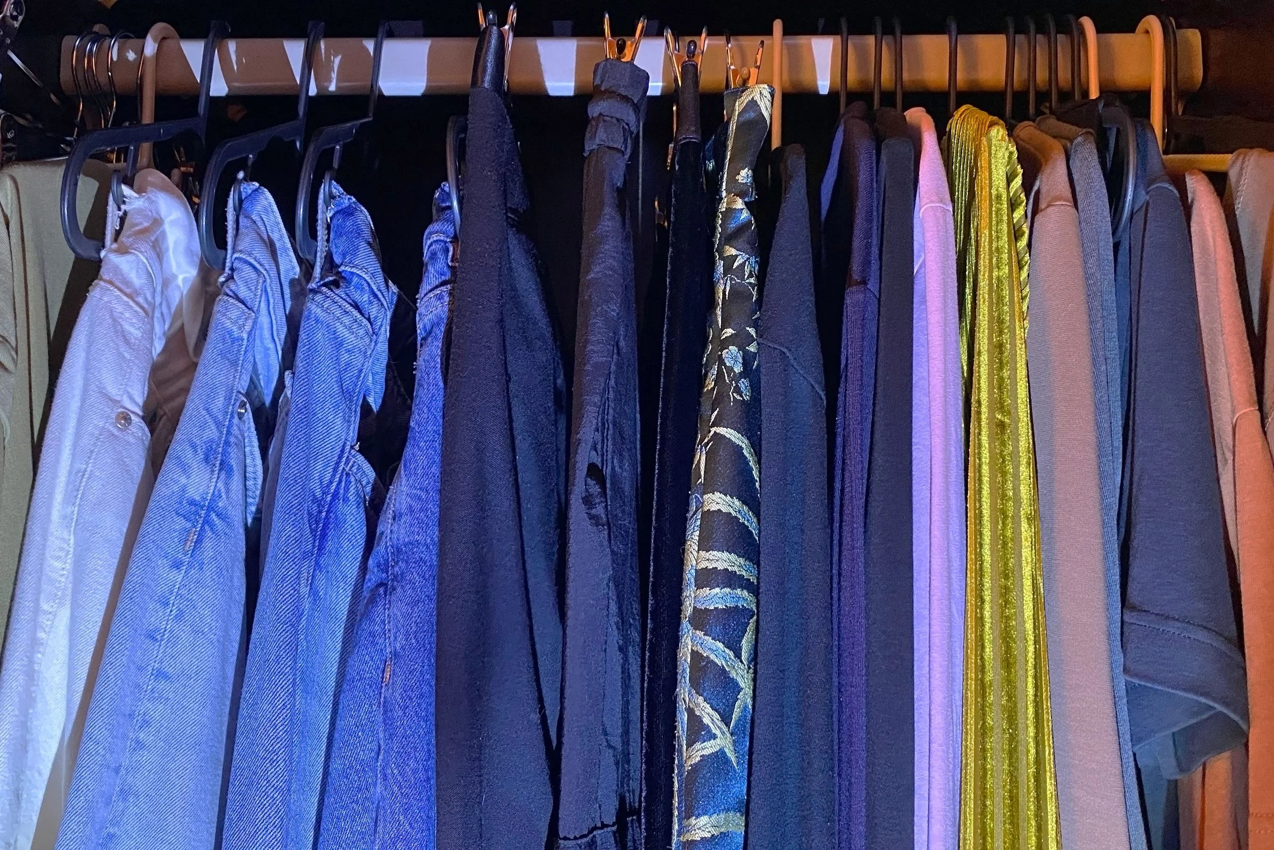 Rack of women's clothing on wooden hangers, including blazers, shirts, and dresses in blues, purples, and gold