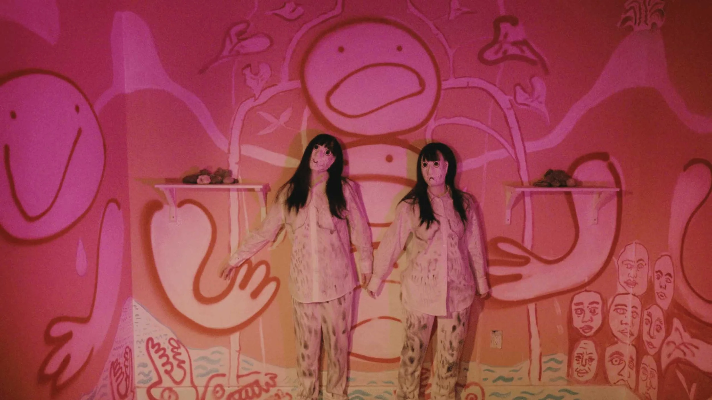 A still image from the short film Stone Skin. Two figures dressed identically, wearing masks and standing against the wall in a room painted with cartoon faces.