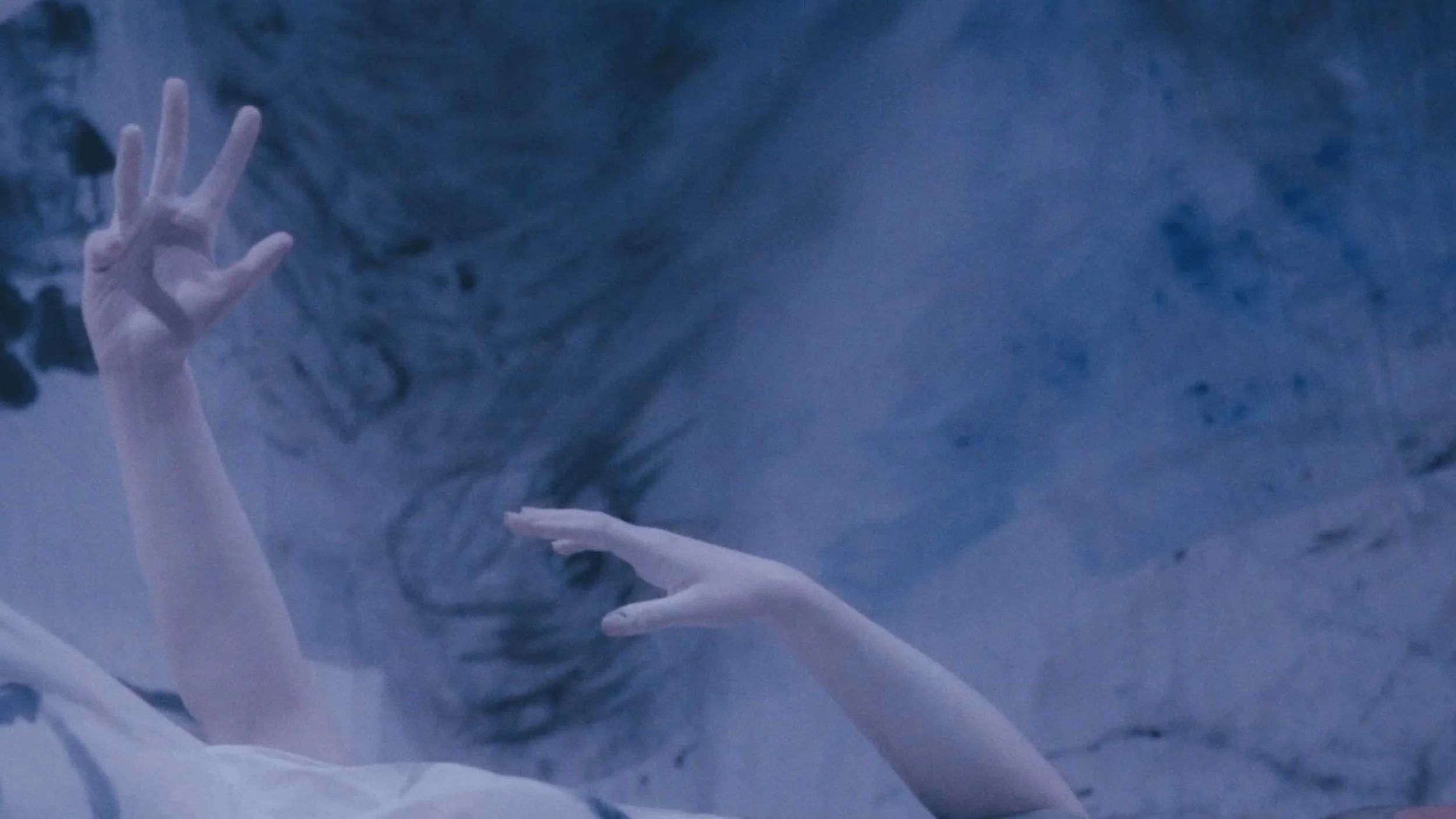 A still image from the short film Stone Skin. Two arms reaching in a fabric ocean.