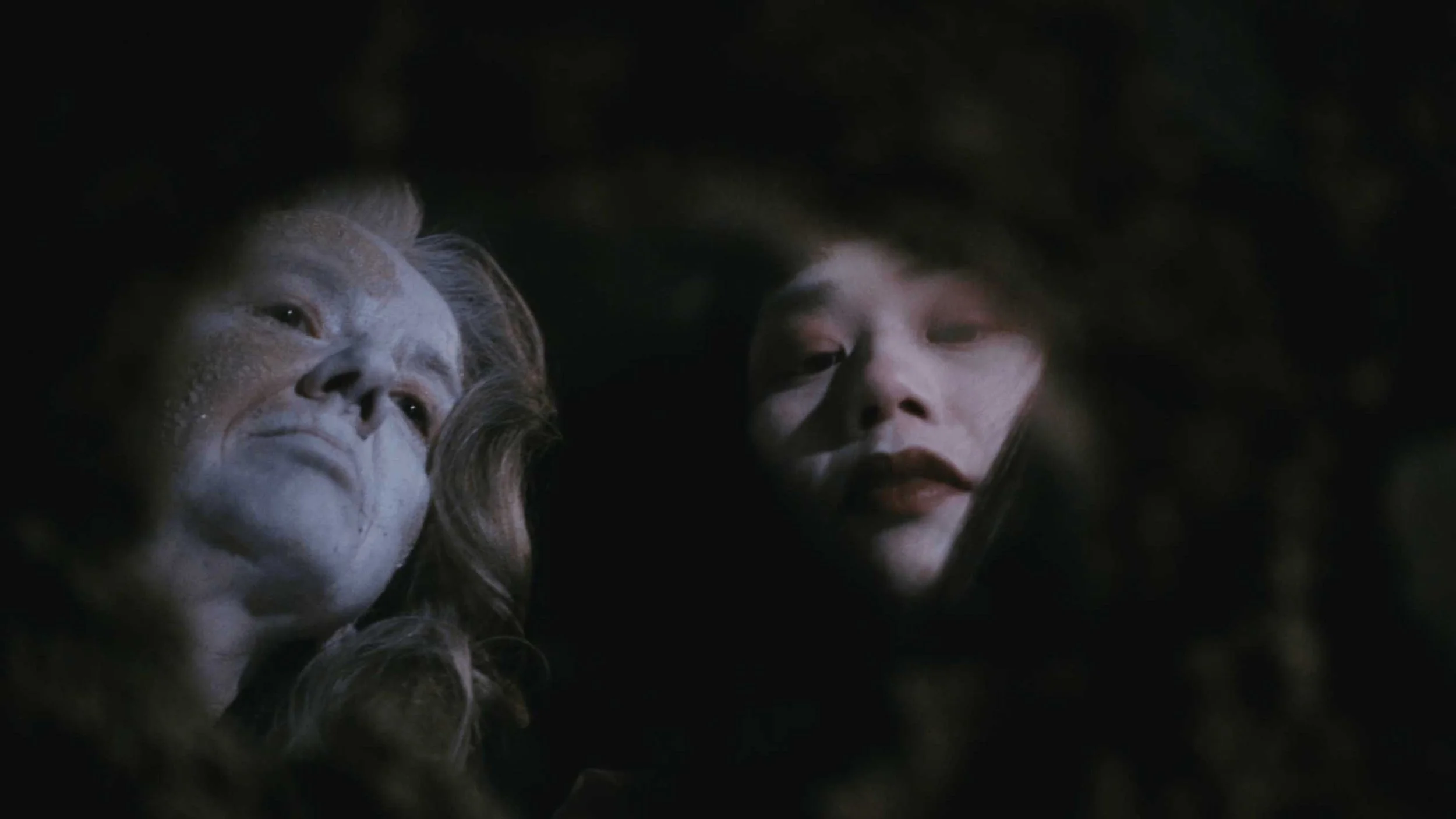 A still image from the short film Stone Skin. Close-up of two women peering into the darkness. 