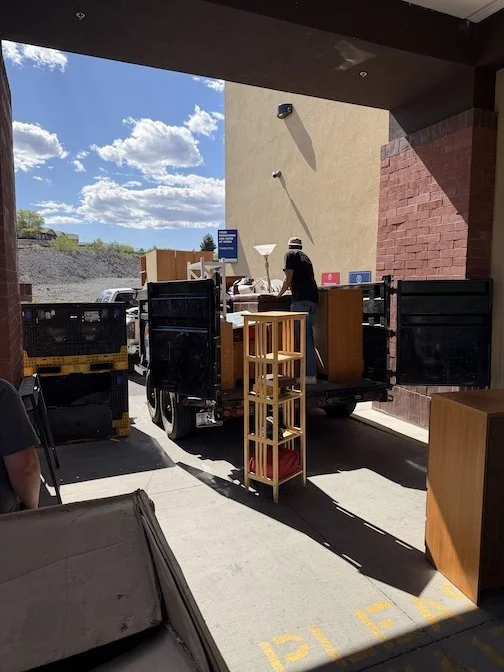 A person unloading donated furniture from a truck outside a building on a sunny day.