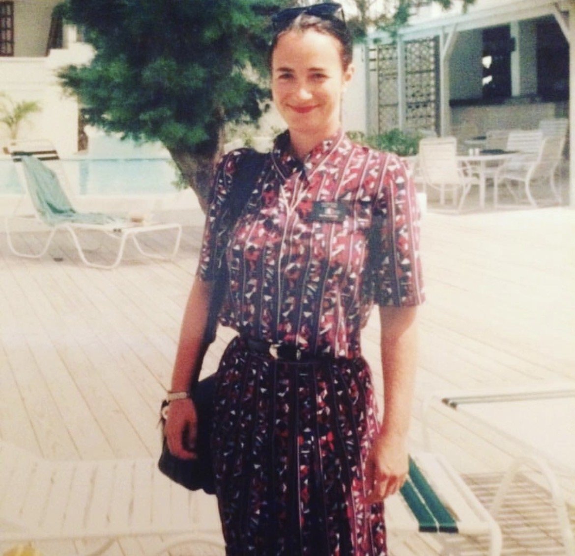 Rebecca stands next to a pool in her cabin crew uniform, smiling at the camera
