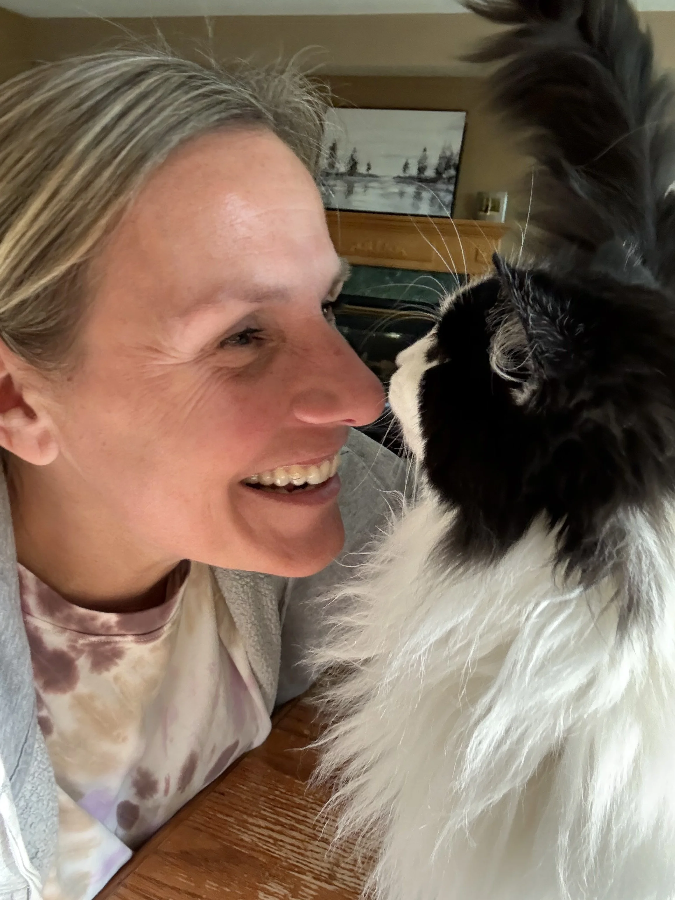 A smiling woman and a black and white cat touching noses.