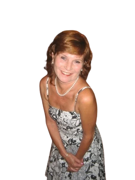 A woman with short red hair smiling, wearing a black and white floral dress and a pearl necklace, standing with hands clasped.