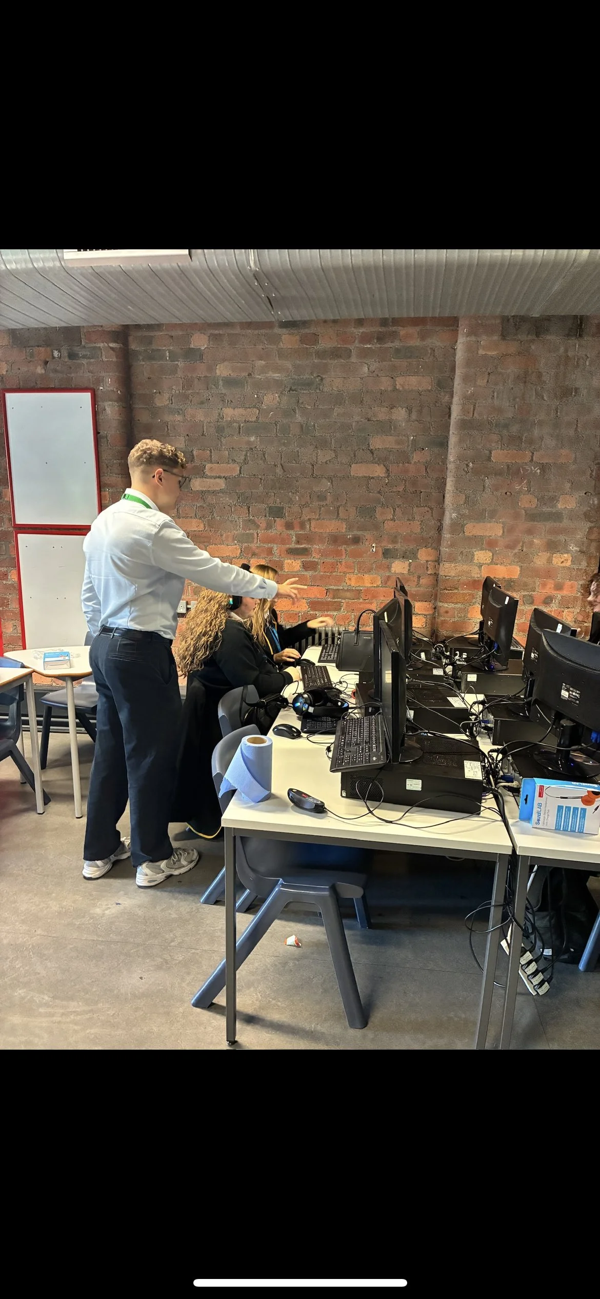 People working at a desk with multiple computer monitors in an office with brick walls.
