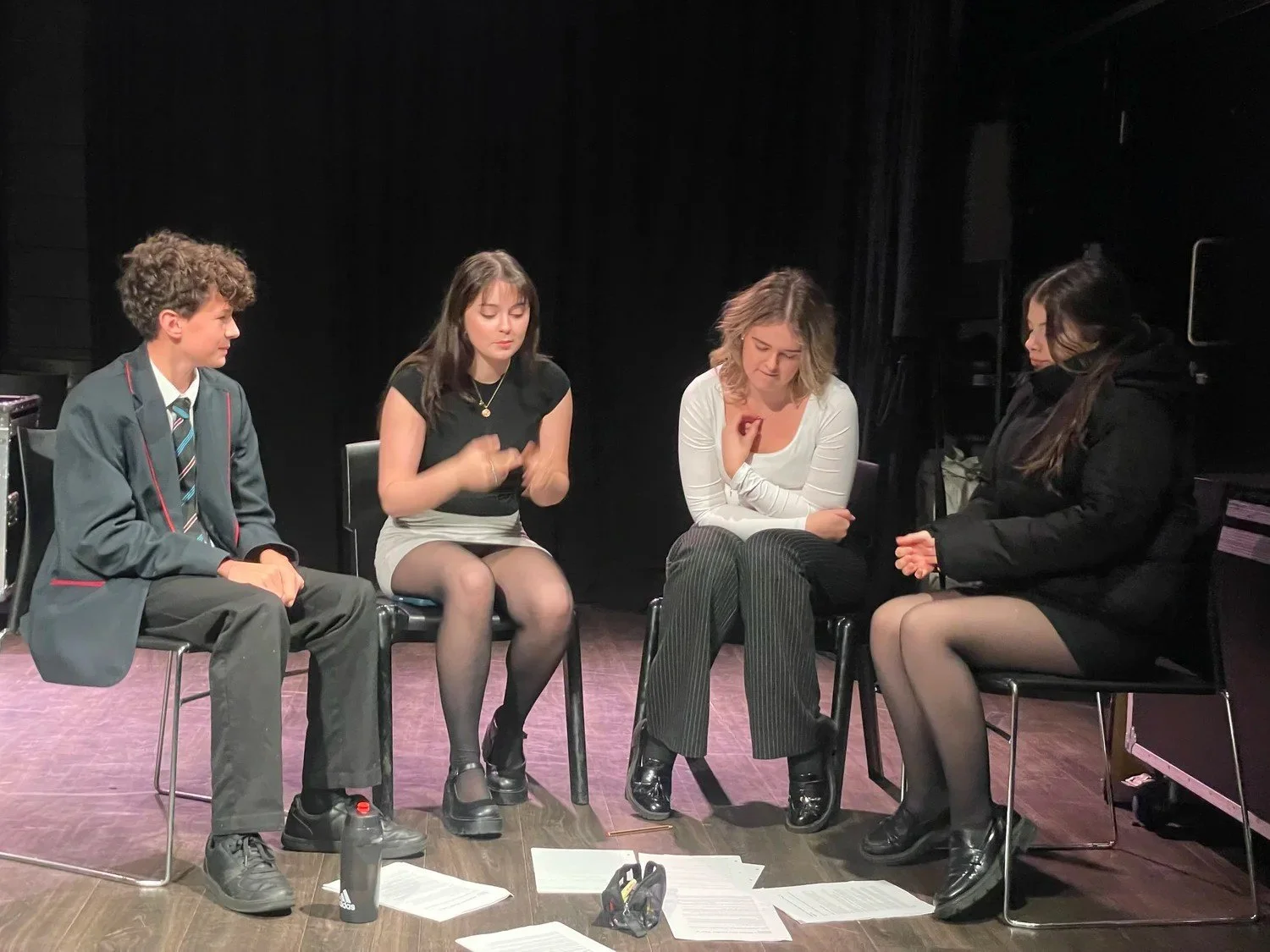 Four young people sit in a row on a stage, reading through scripts together during a rehearsal for the Beat Modules films.