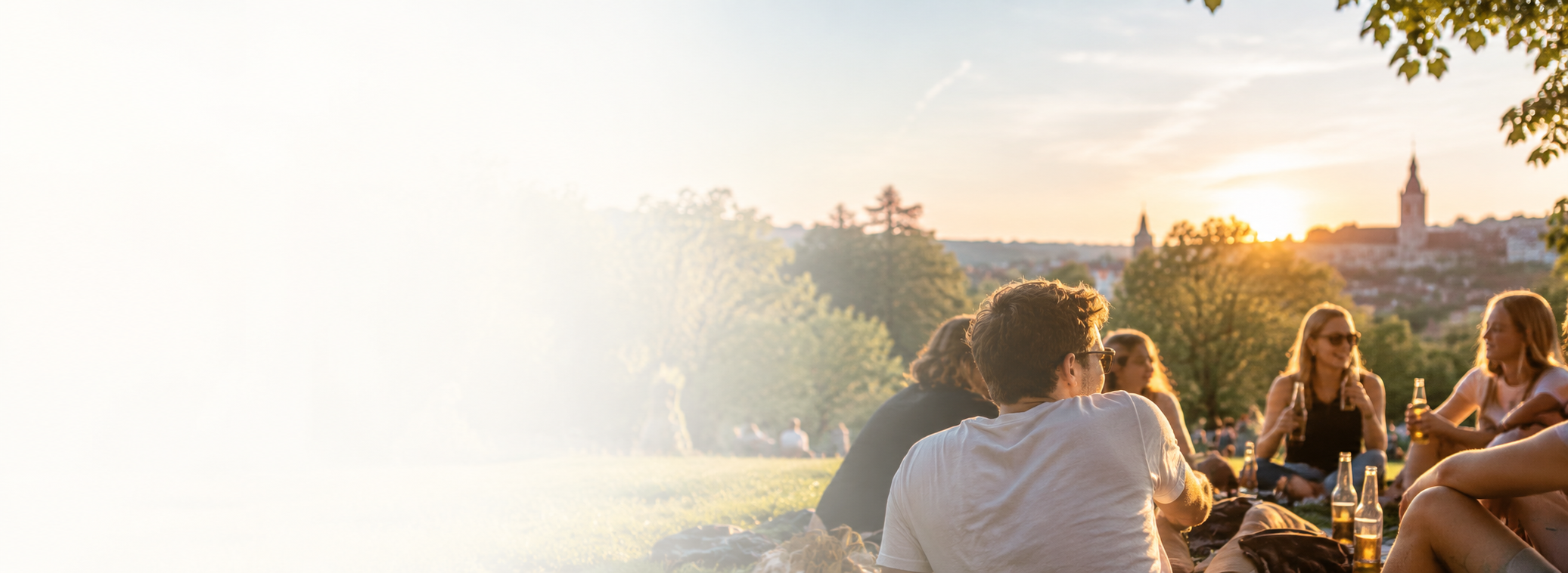 Gruppe von jungen Menschen, die im Park bei Sonnenuntergang sitzen und Bier trinken.
