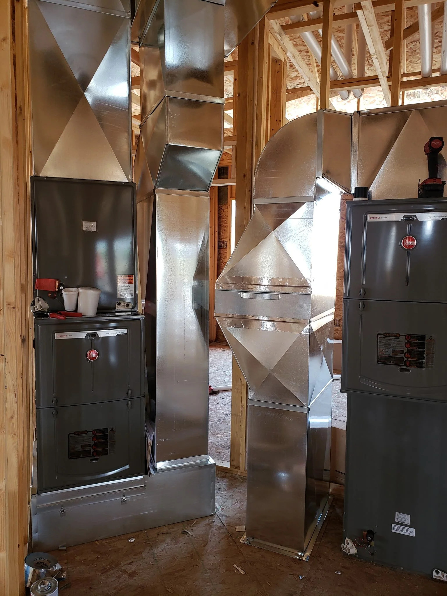 An unfinished room under construction with exposed wooden framing and electrical pipes, featuring metallic HVAC ductwork and electrical panels.