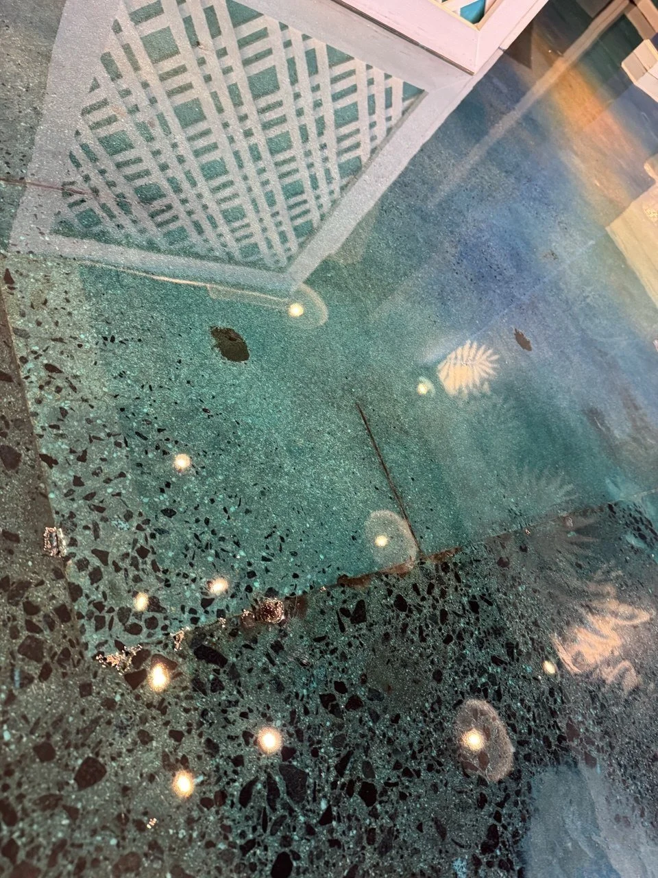 Reflection of a white lattice pattern in a wet, speckled green and black terrazzo floor.