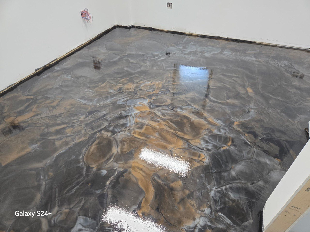 A room with a newly poured, shiny, dark marble floor with white and tan epoxy
