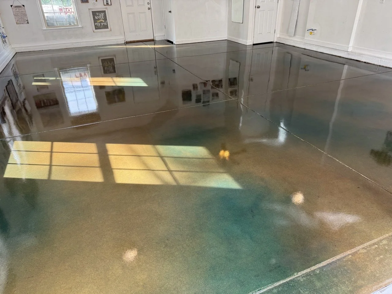 A room with polished, shiny concrete floors reflecting windows and ceiling lights, white walls, and framed artwork.