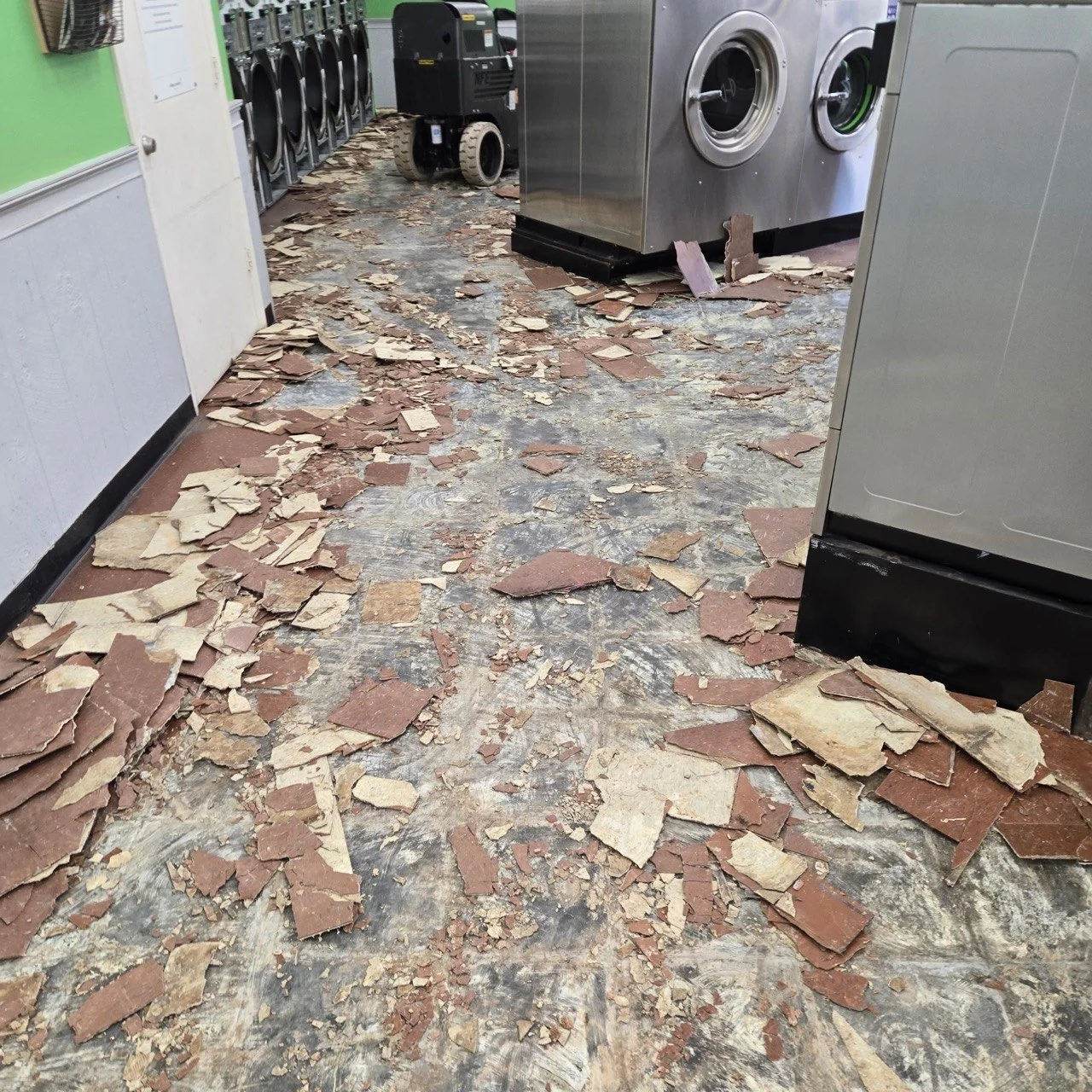 Broken tiles scattered across the floor of a laundry room with washing machines and dryers lining the wall.