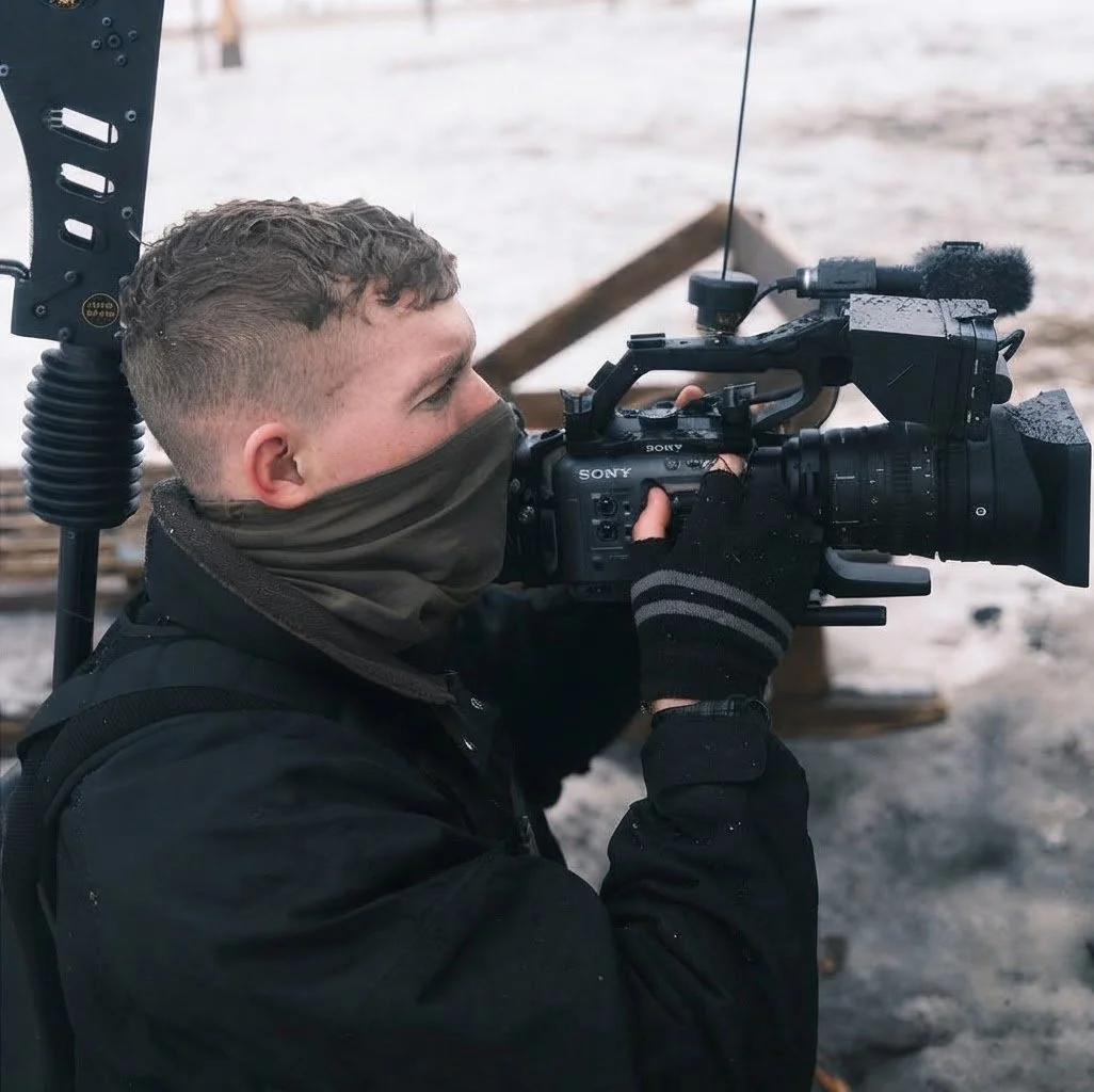 Person filming with a professional Sony video camera outdoors in cold weather, wearing a face covering and gloves.