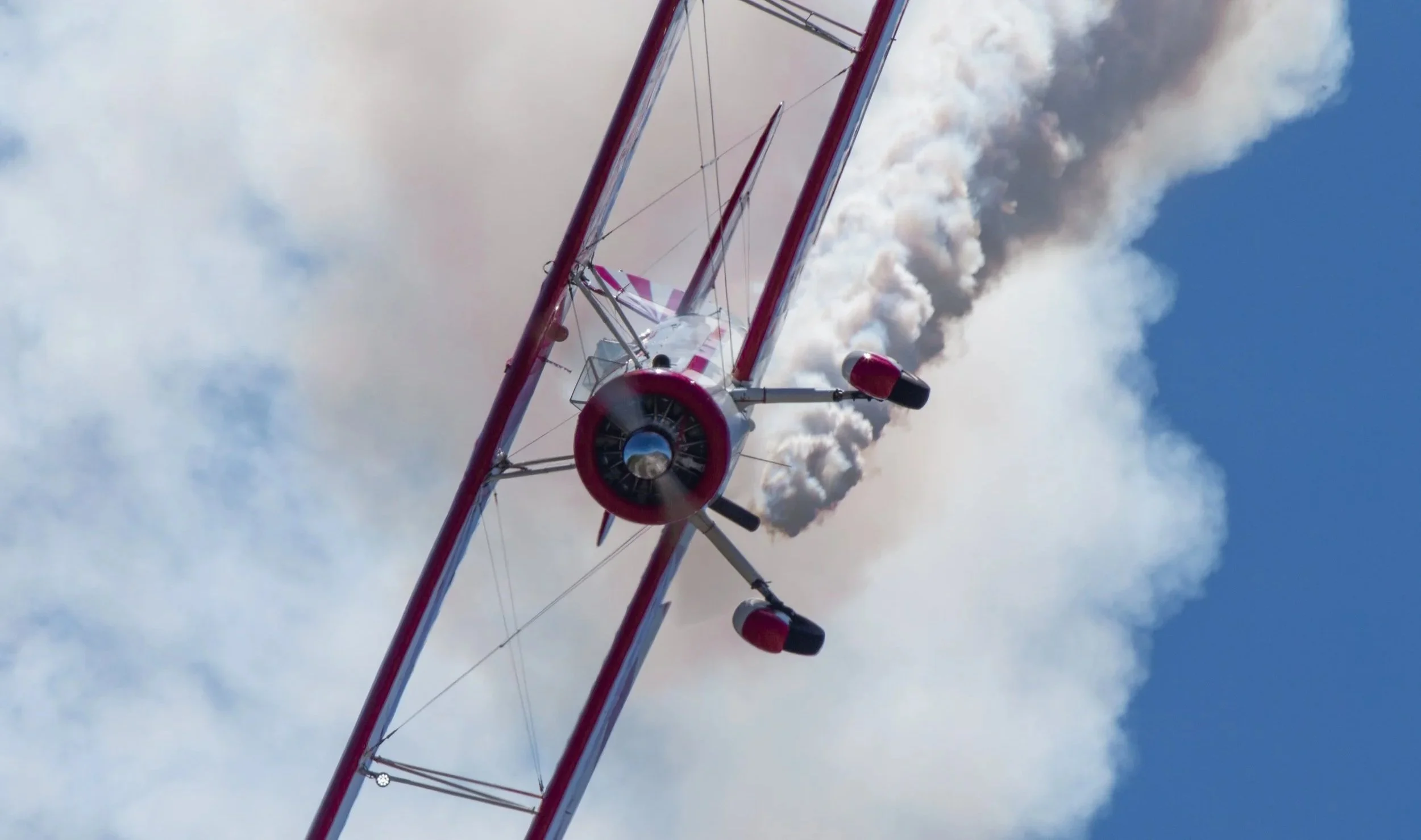 Red and white biplane flying through a cloudy sky.
