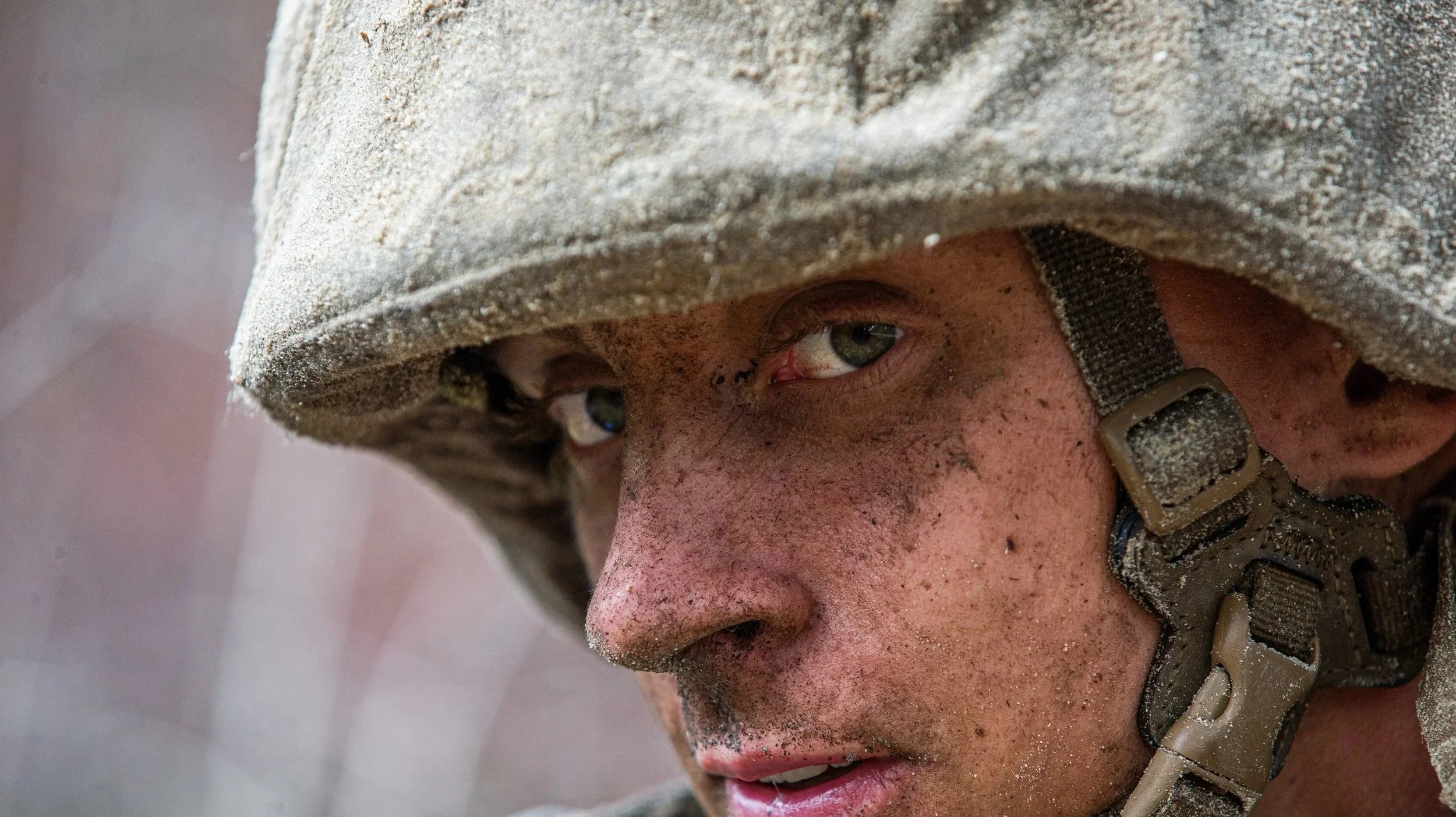 Close-up photo of a person wearing a muddy helmet and climbing gear, with a focus on their gritty, dirt-streaked face and intense expression.