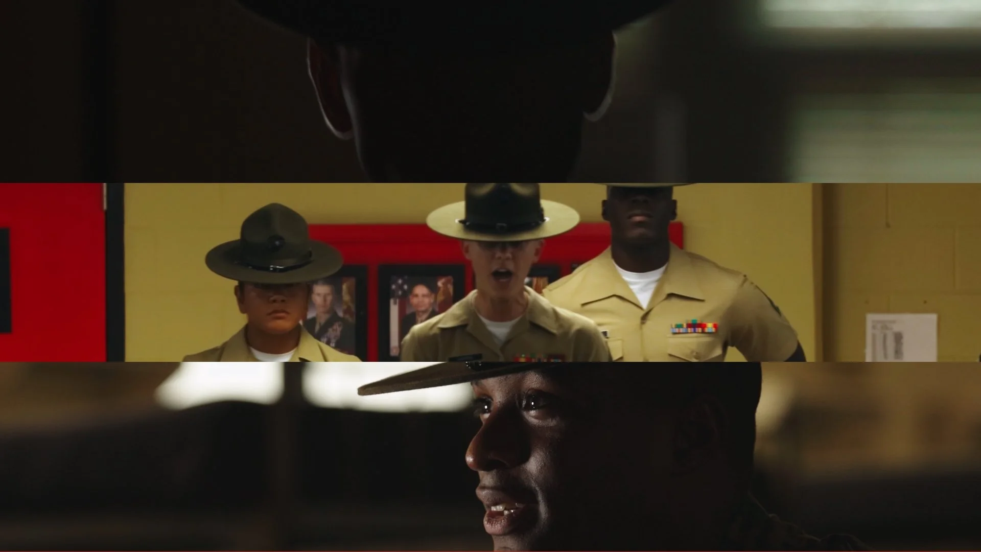 Scene from a military setting showing three soldiers in uniform, with two wearing hats and one acting as a speaker, in a room with framed pictures on the wall.