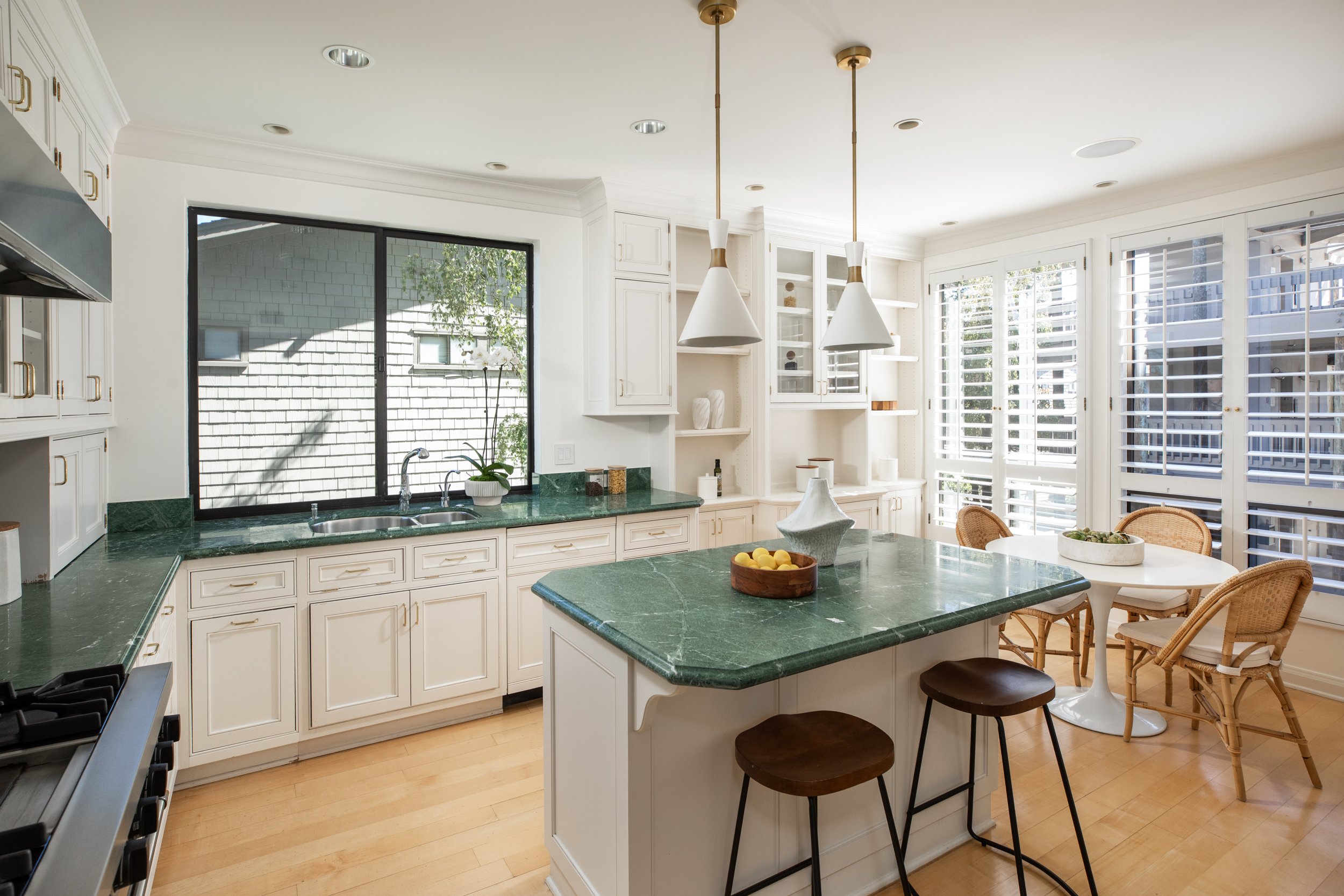 Kitchen with white cabinets, green marble countertops, a kitchen island, and large windows with white shutters.