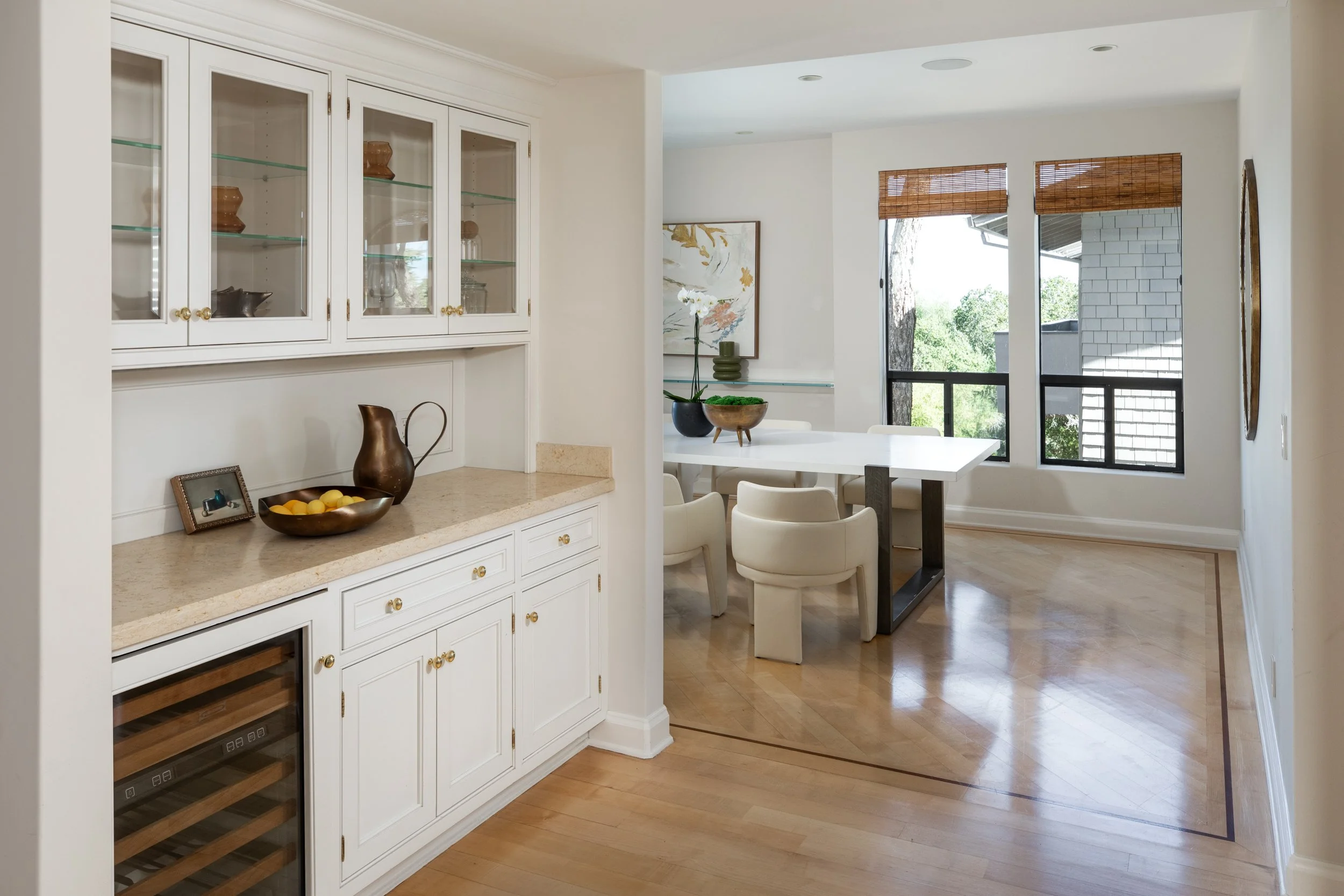 A bright dining area with large windows, a white dining table, white chairs, and decorative art on the walls.