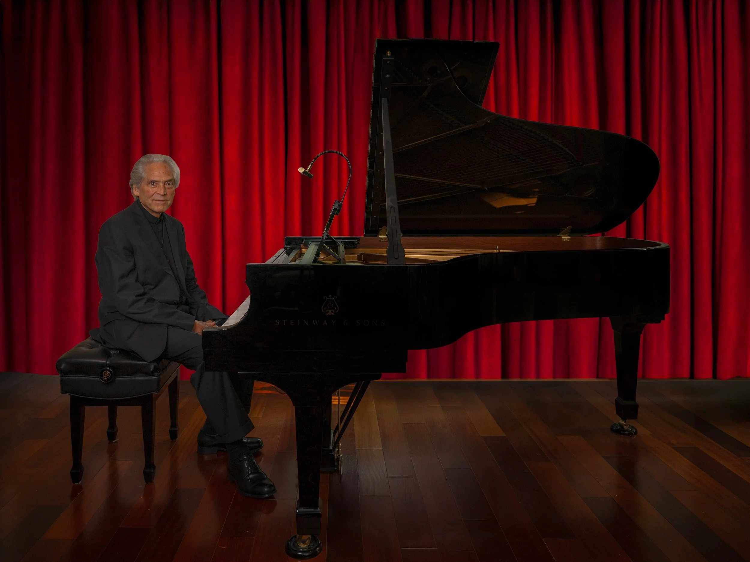 David Masterson, Piano Pinehurst instructor is seated at a black Steinway grand piano on a stage with red curtains.