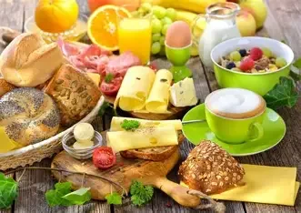 Frühstückstisch mit Brot, Käse, Eiern, Obst, Joghurt, Kaffee und Süßigkeiten