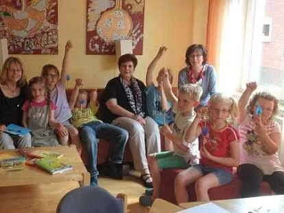 Mehrere Kinder und zwei Erwachsene sitzen in einem Raum an einem Tisch, einige Kinder heben die Hand, vermutlich bei einer Fragerunde.