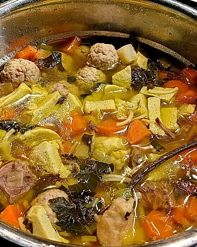 Ein Topf mit Gemüsesuppe, gefüllt mit Karotten, Sellerie, Zwiebeln, Knoblauch, und Fleischbällchen.