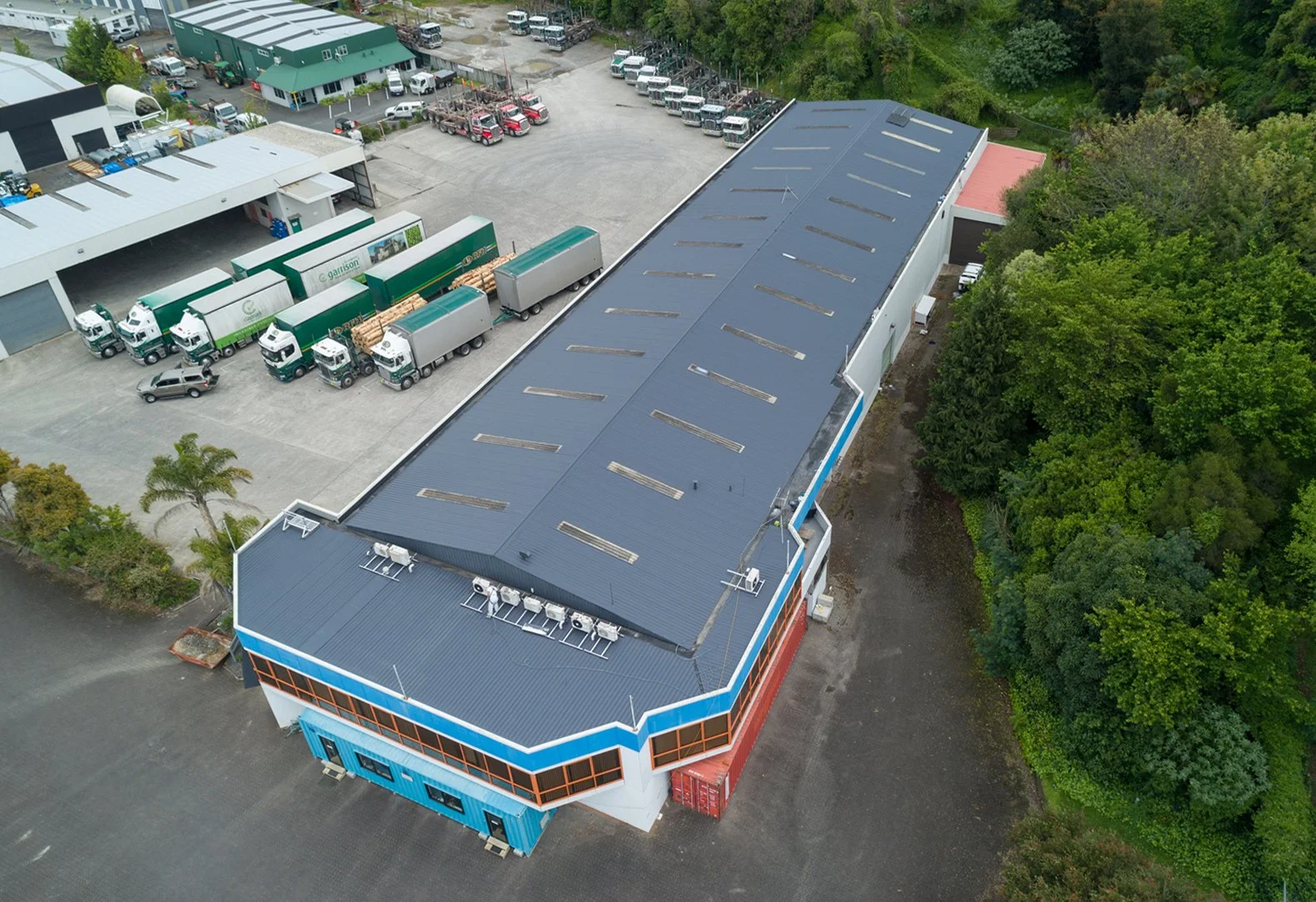Aerial view of an industrial warehouse and commercial trucking yard surrounded by dense greenery.