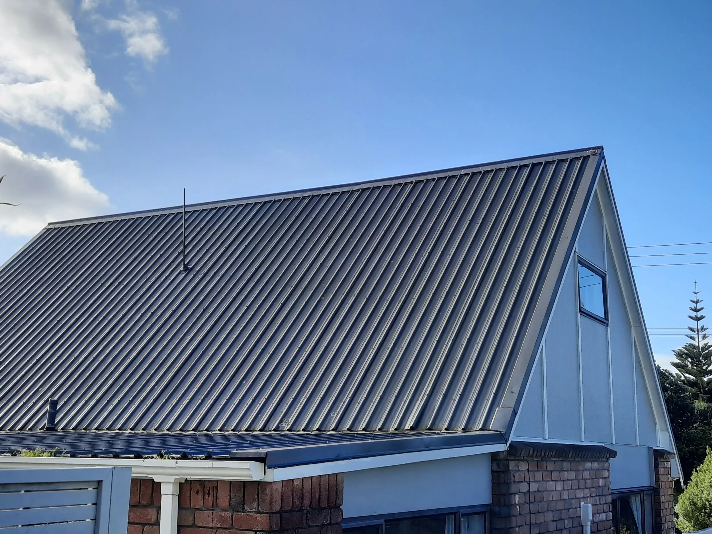 Close-up of a dark corrugated metal gable roof on a brick house beneath a blue sky
