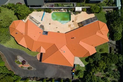 Aerial view of a large red-roofed house with a swimming pool, landscaped yard, and driveway