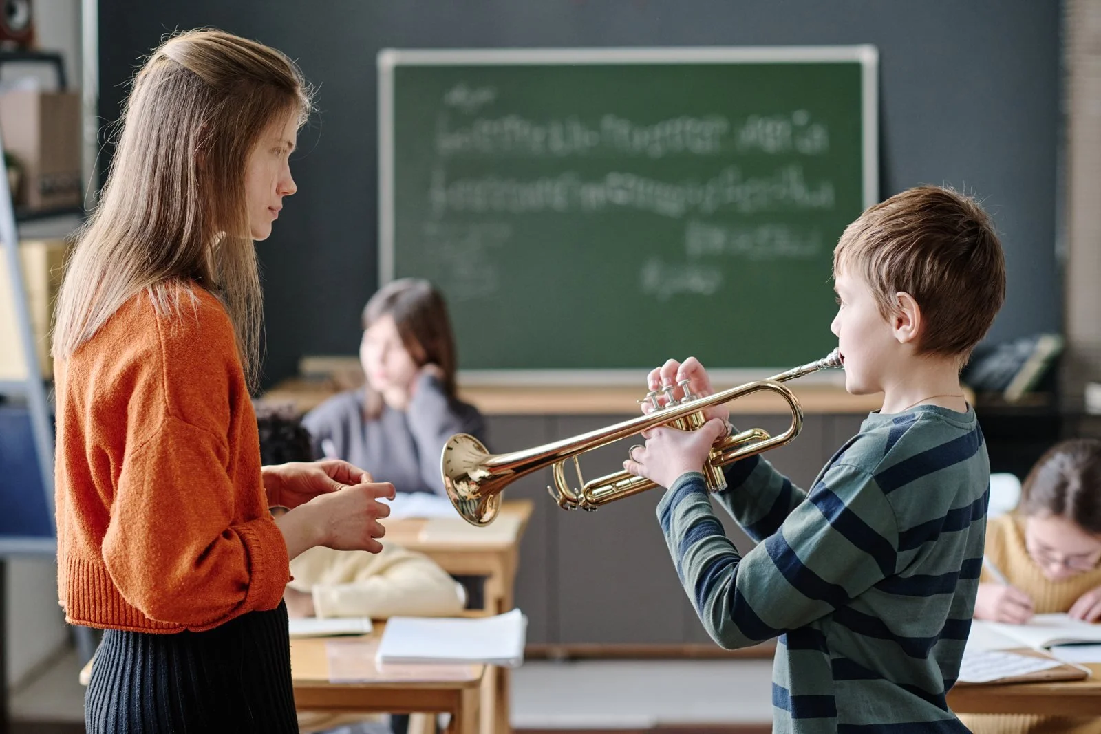 A teacher listening to a pupil play the trumpet in class