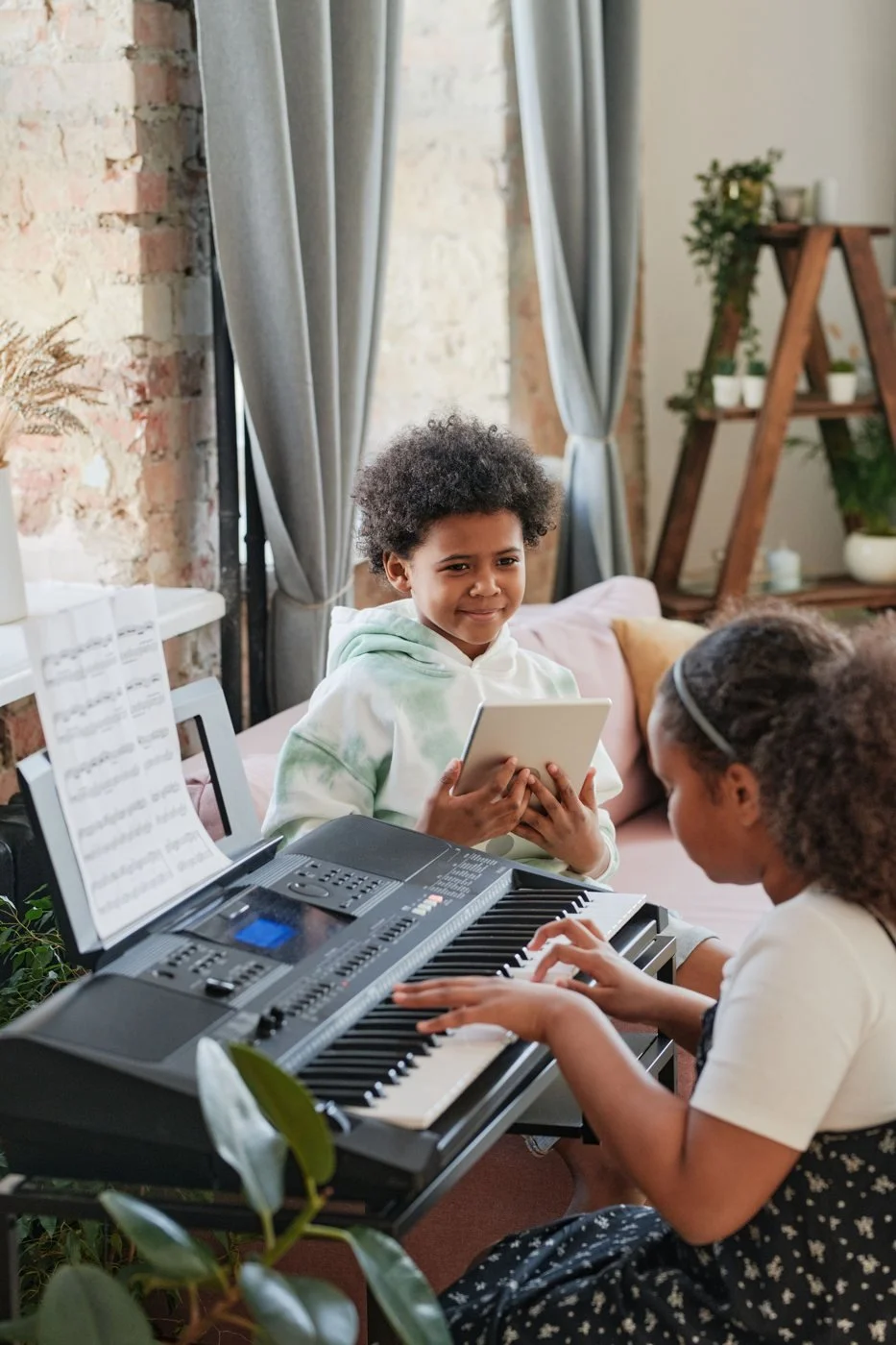 Two children practising music together with a keyboard and a tablet