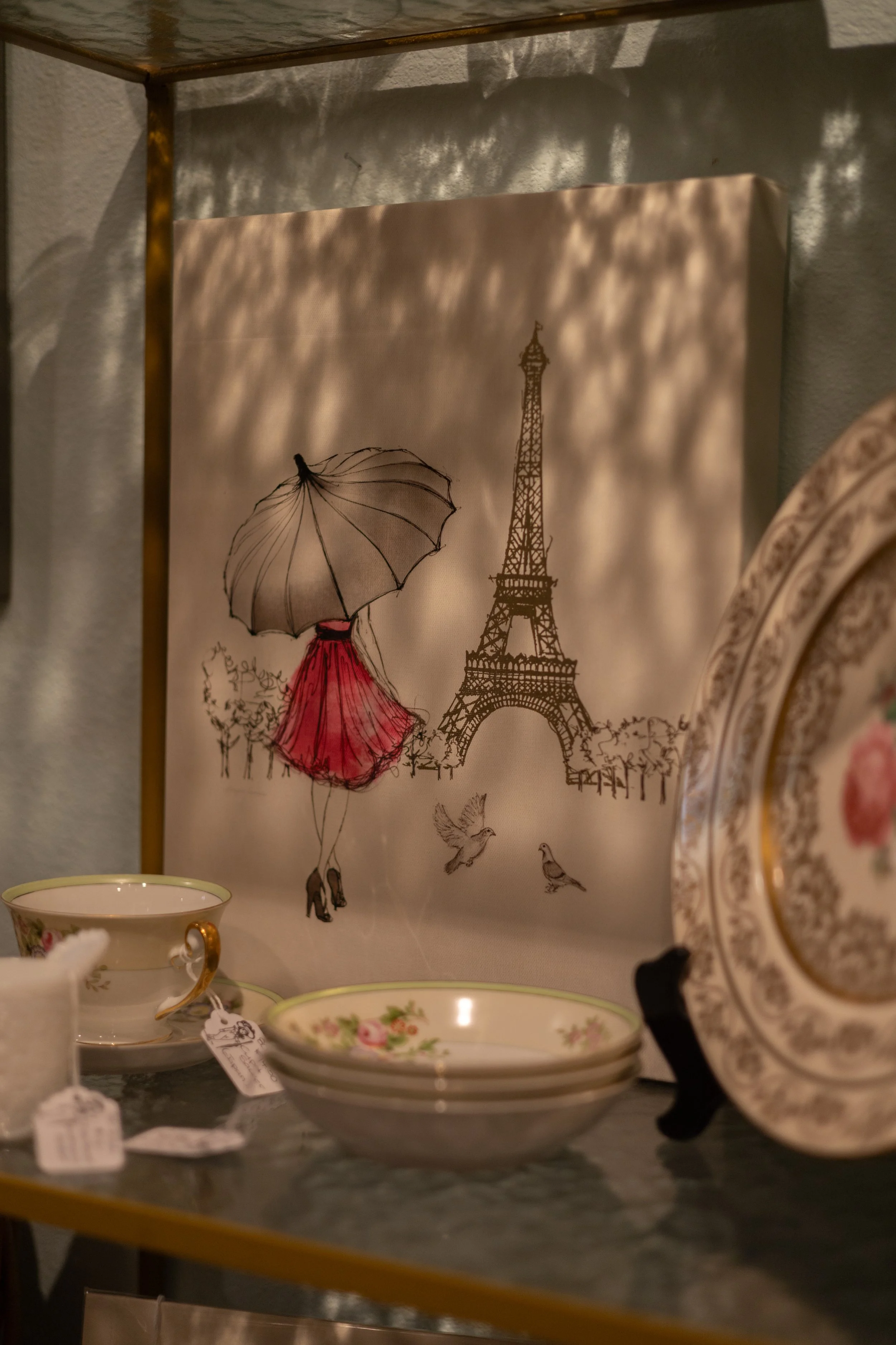 Decorative wall hanging featuring a sketch of the Eiffel Tower, a woman with an umbrella and red dress, and birds flying.