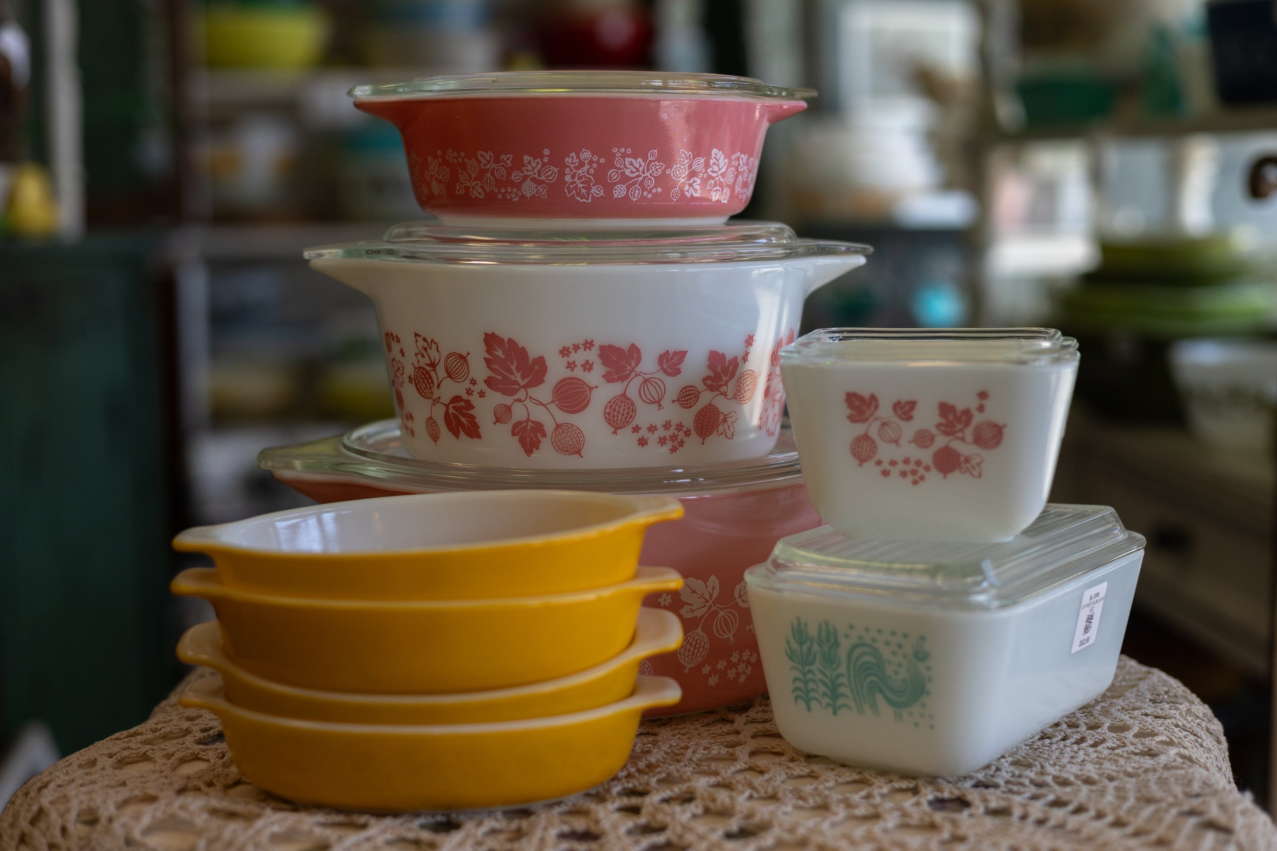 Stacked colorful ceramic bowls and small containers with floral and fruit patterns on a lace tablecloth.
