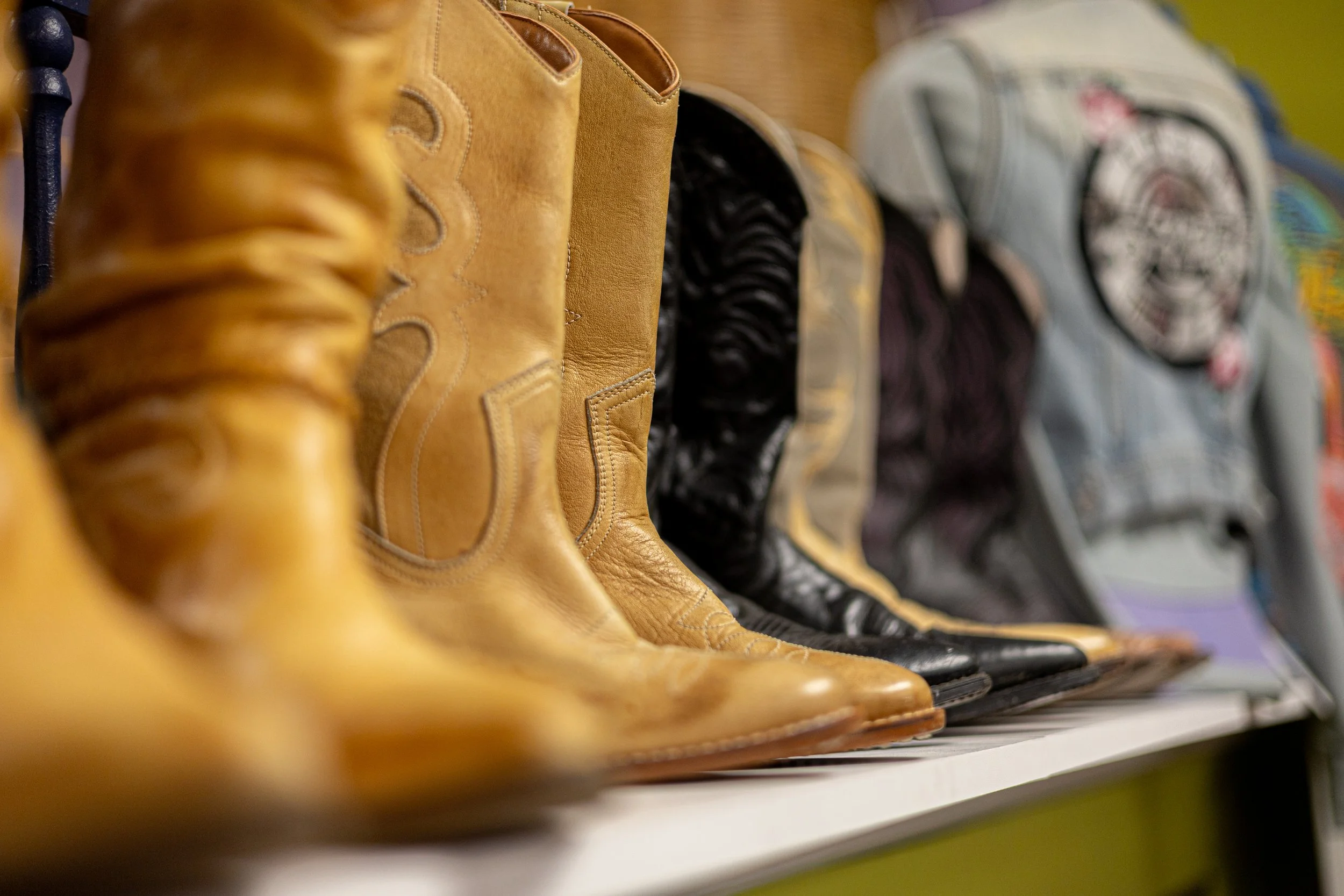 A row of various shoes on display, including tan leather boots and sneakers, on a store shelf.