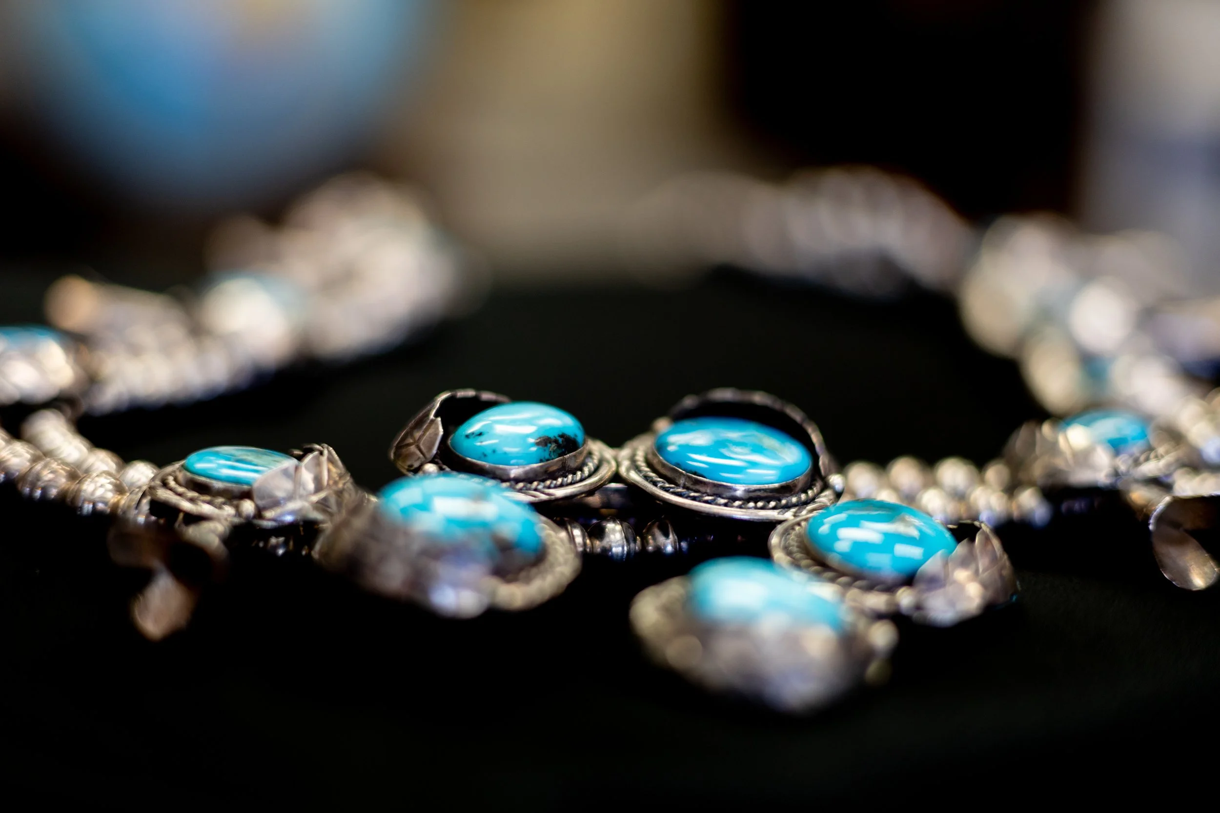 Close-up of a silver necklace with oval-shaped turquoise stones on a black background.