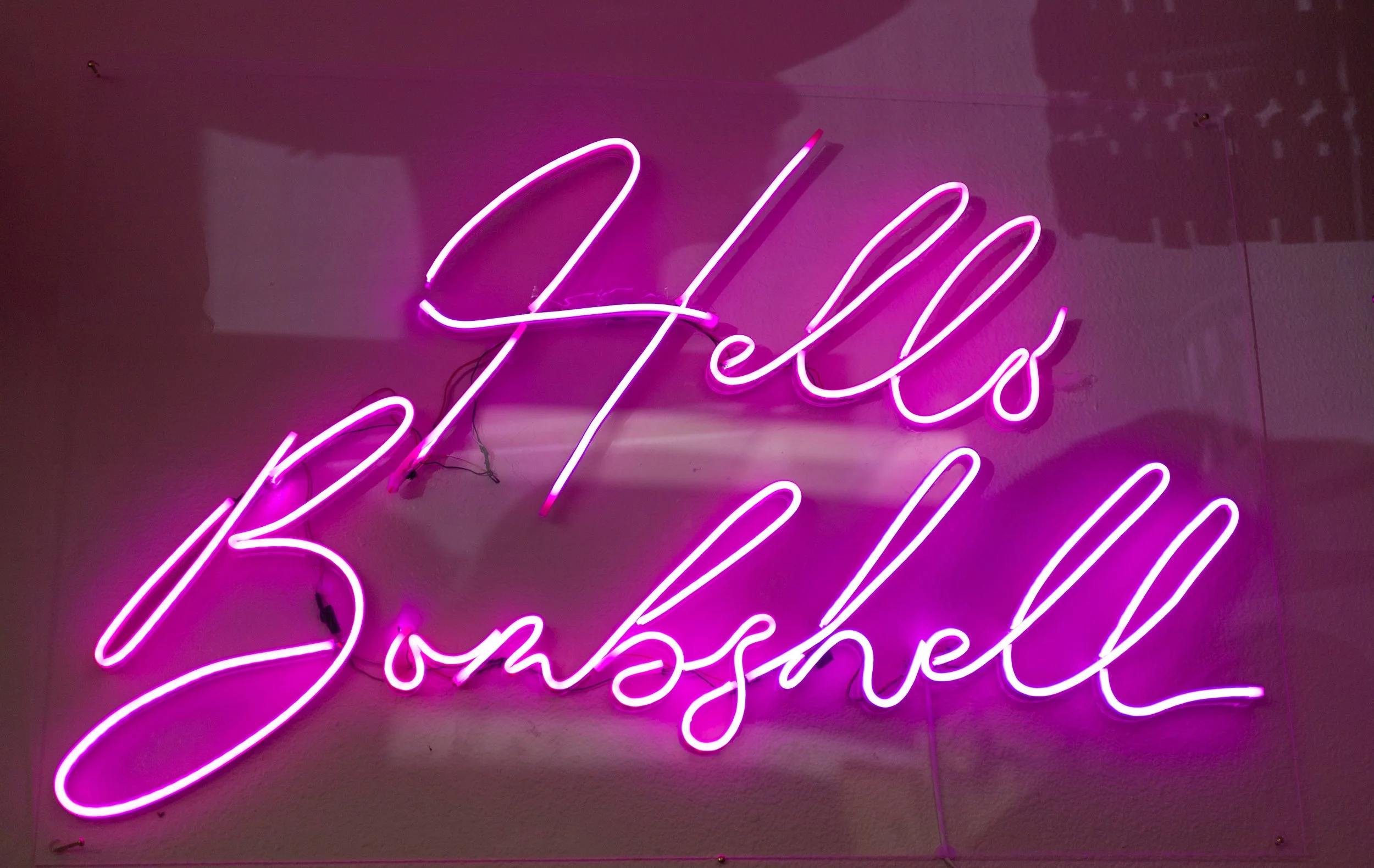 Pink neon sign on a wall that reads 'Hello Beautiful' in cursive script.
