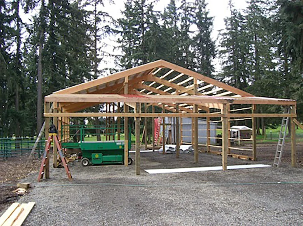 Under construction wooden building frame in a forested area with construction tools and equipment.