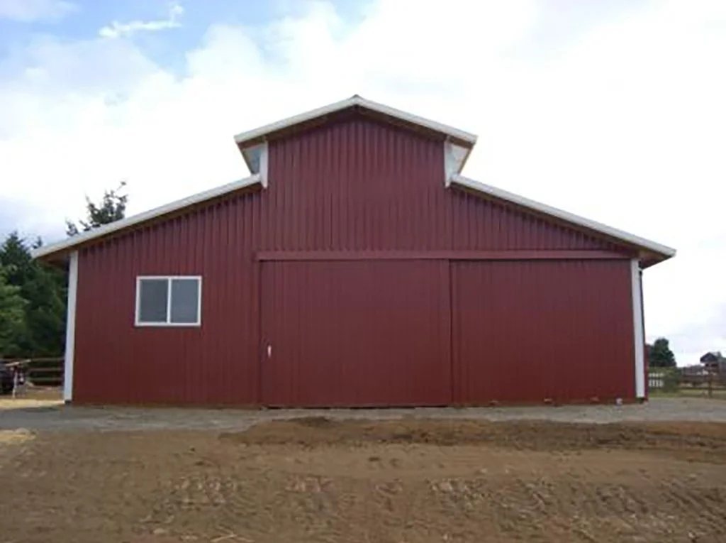 A red barn with a white-framed window and sliding door, surrounded by dirt ground, under a cloudy sky.