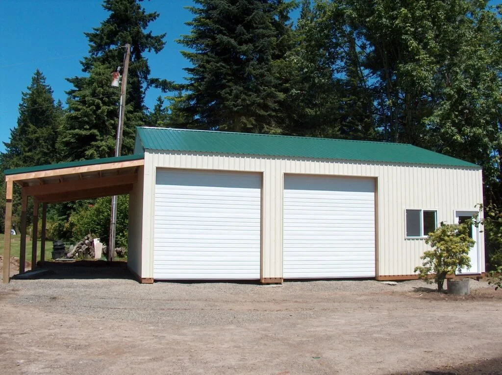 A metal building with two garage doors, a small window, and a side door, situated in a rural area with trees and clear blue sky.