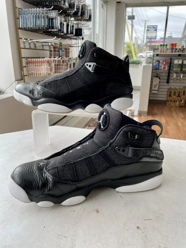 Pair of black Nike Air Foamposite sneakers with white soles on a white surface, inside a store with shelves and large windows in the background.
