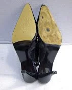 Pair of black and yellow high-heeled shoes with pointed toes, photographed from the bottom.