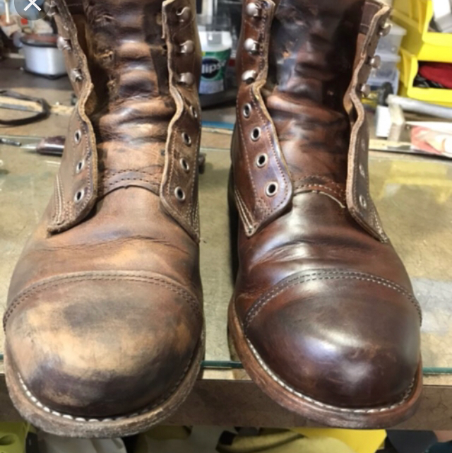 Comparison of two leather work boots, one worn and scuffed, the other new and polished, on a workbench with tools and supplies in the background.