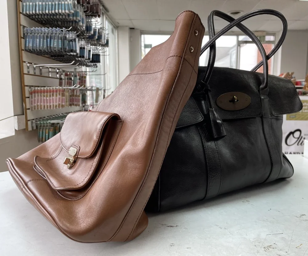 A large black leather handbag and a smaller brown leather handbag placed on a white surface in a store with a display of sewing supplies in the background.