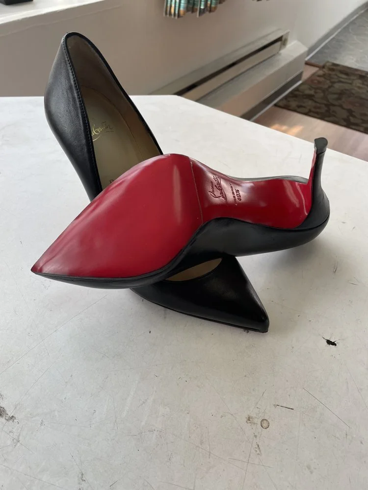 A pair of high-heeled shoes, with one shoe on its side and the other standing upright. The shoes are black and red leather.