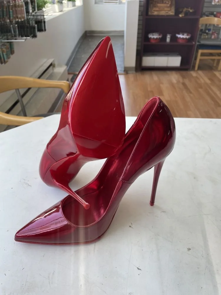 Red high-heeled shoes with a transparent design, arranged to resemble a pair of shoes on a white surface.