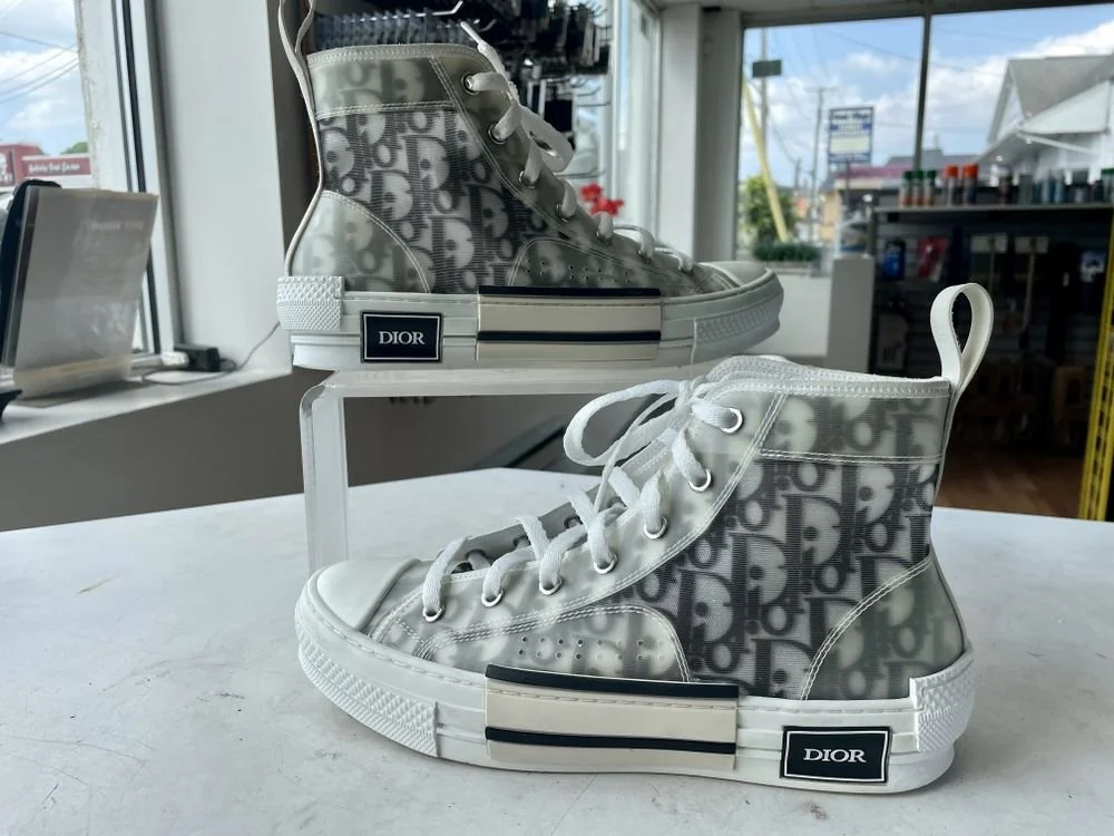 A pair of designer high-top sneakers with a clear, transparent material and a black and white logo pattern, displayed on a small white stand inside a store.