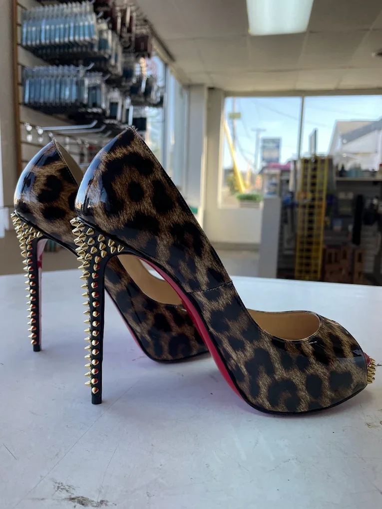Leopard print high-heeled shoes with gold spikes on the heels and toe, displayed on a white surface in a store.