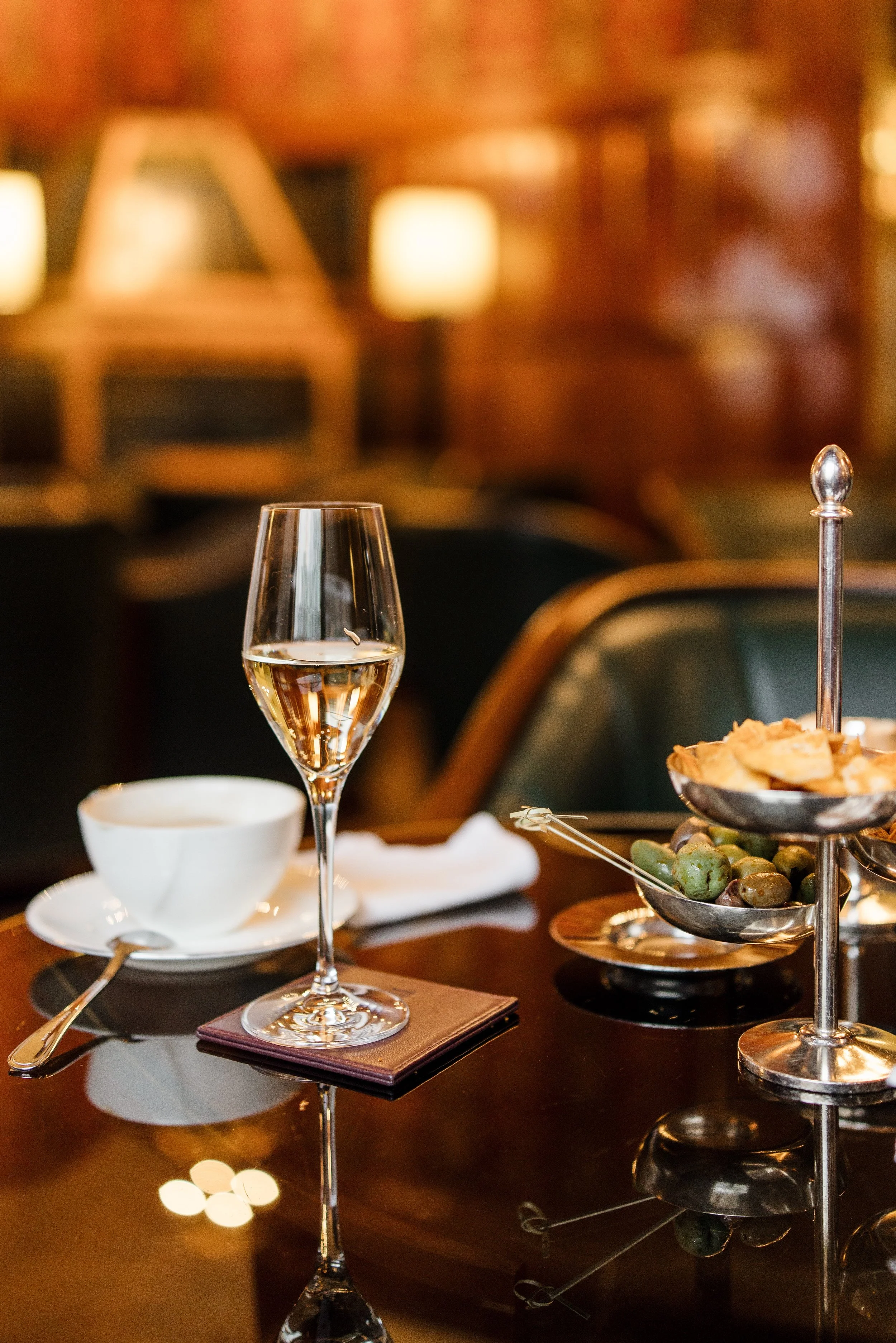 Elegant glass of sparkling wine with gourmet appetisers and olives in an intimate restaurant lounge, evoking a sophisticated dinner date with a luxury London companion.